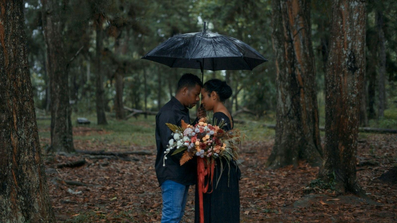 A couple under an umbrella on a forest floor of fallen leaves in the rain