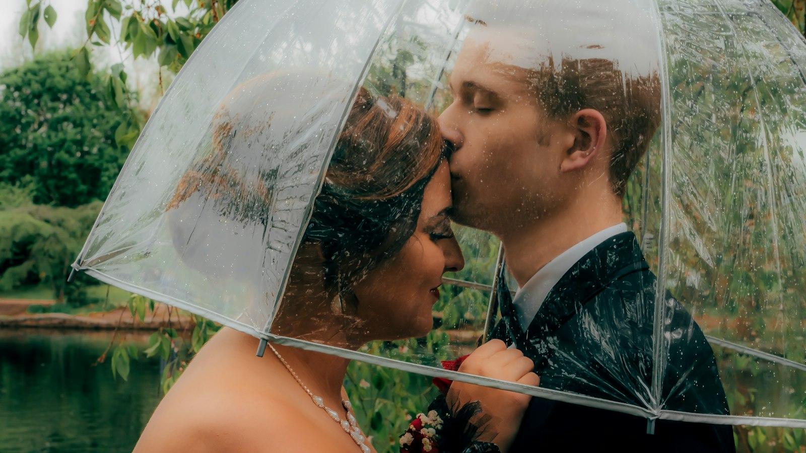 A couple sharing a clear umbrella outside on a rainy wedding day