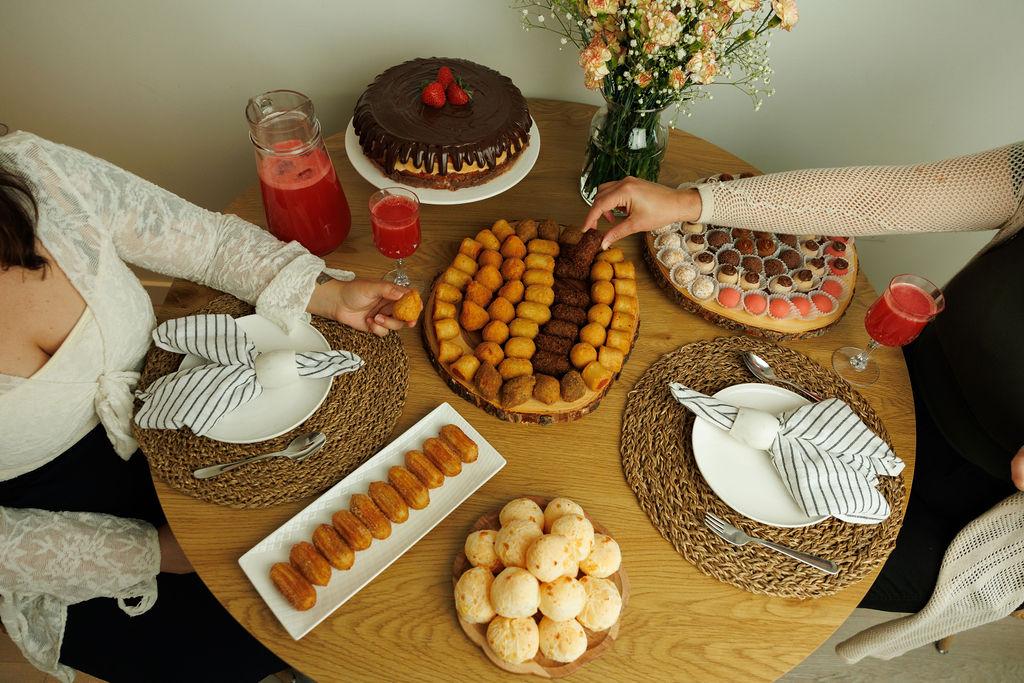 A table of Brazilian party food from Gimme Bakery in Vancouver: coxinhas, brigadeiros in paper cups, cheese bread and a chocolate cake topped with strawberries.