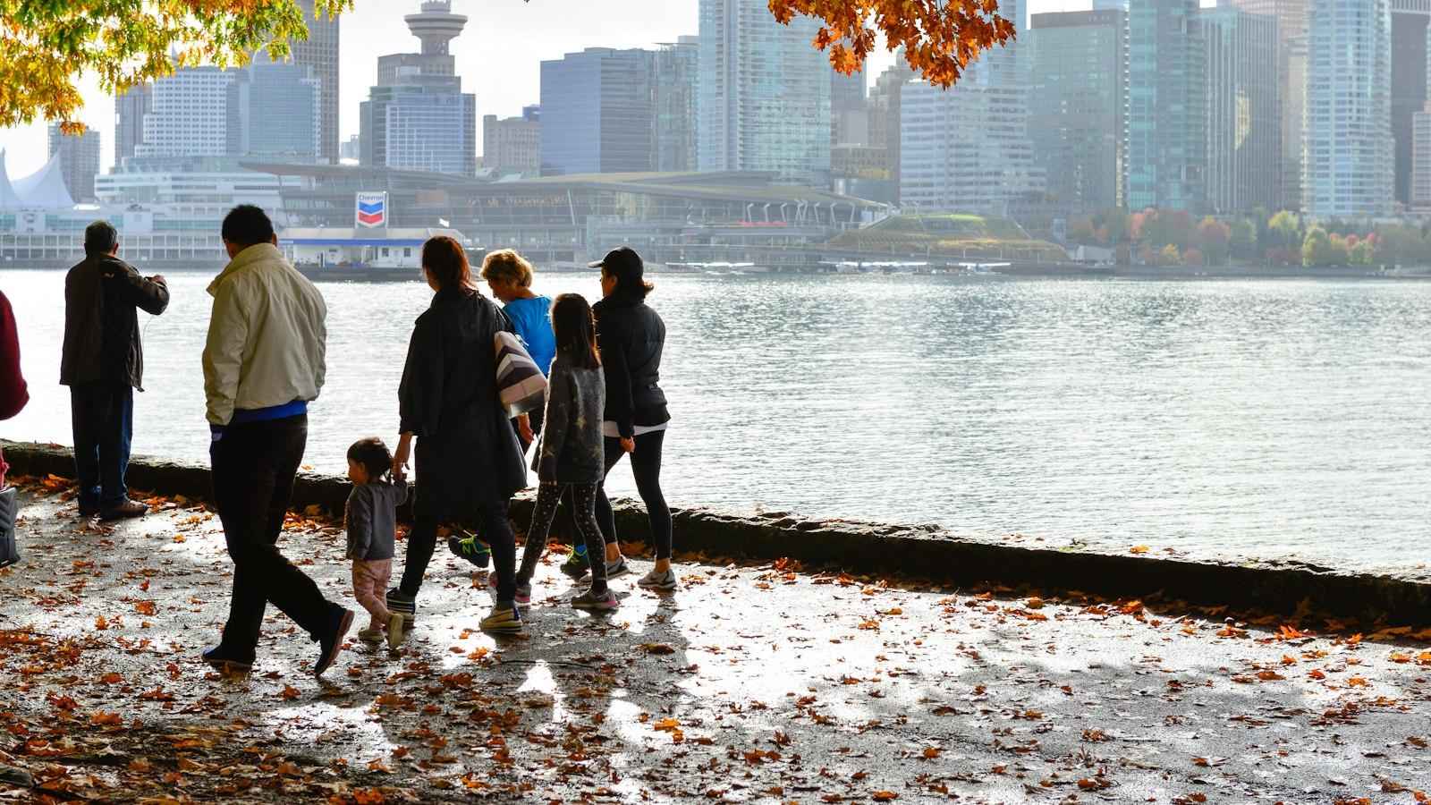 People walking the Stanley Park seawall in Vancouver after an autumn rain, with the downtown skyline hazy in the distance