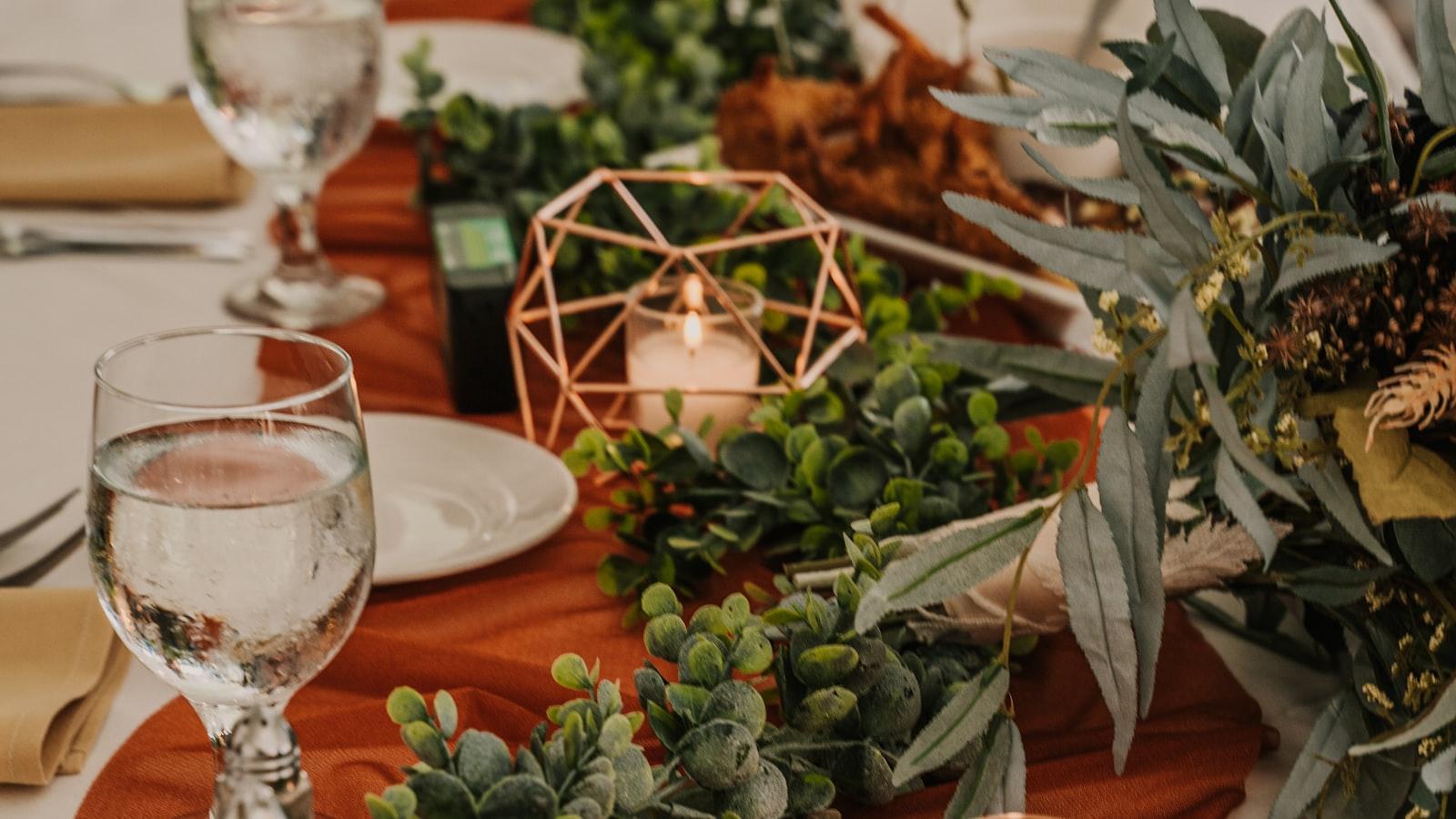 A candle-lit dinner table dressed with greenery and a rust-coloured runner