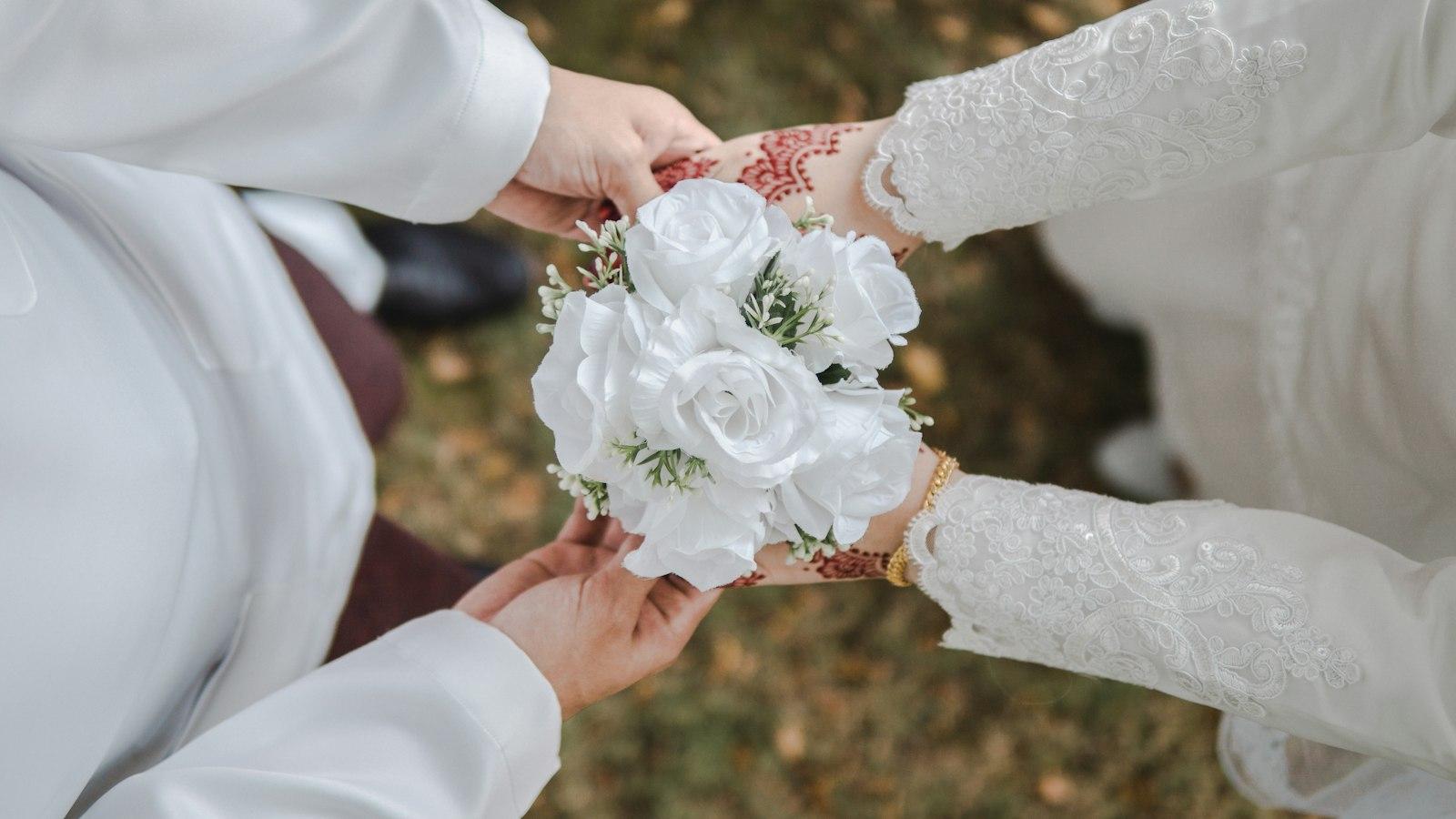 A close-up of hands holding a white rose bouquet